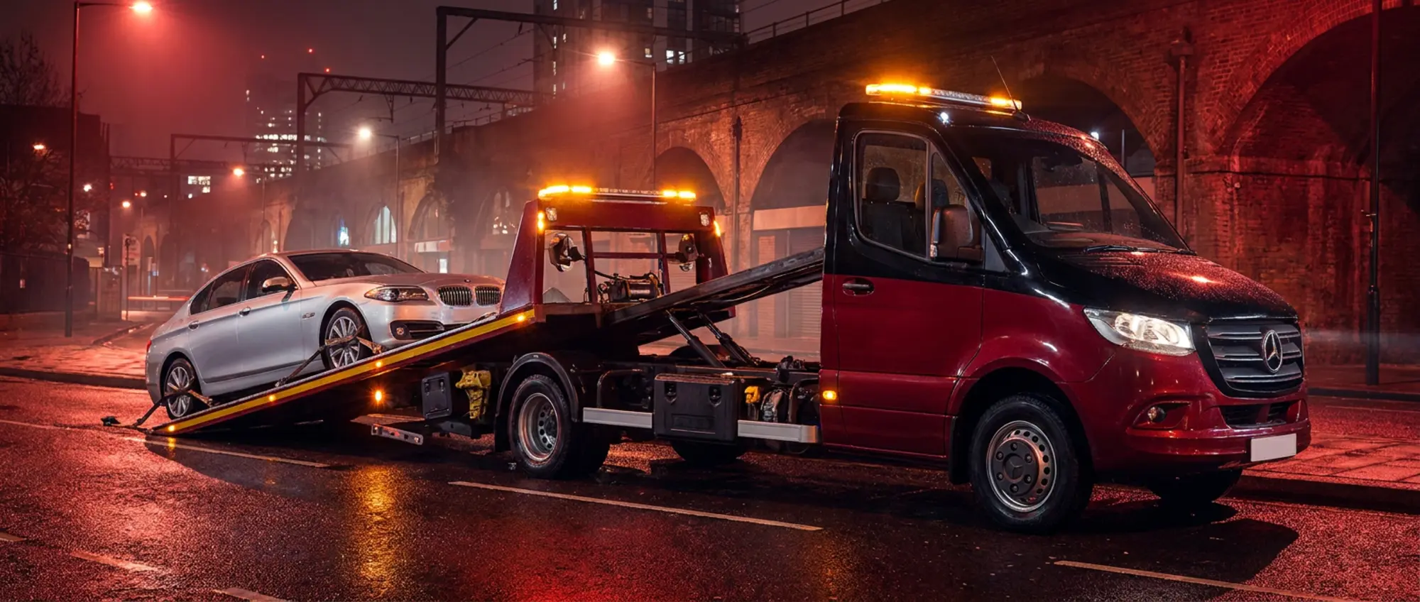 Recovery truck loading a car onto its flatbed at night